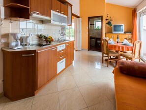 A modern kitchen with wooden cabinets, a built-in microwave, and a dining area with a table set for two. - Apartments Vanessa (Crikvenica)