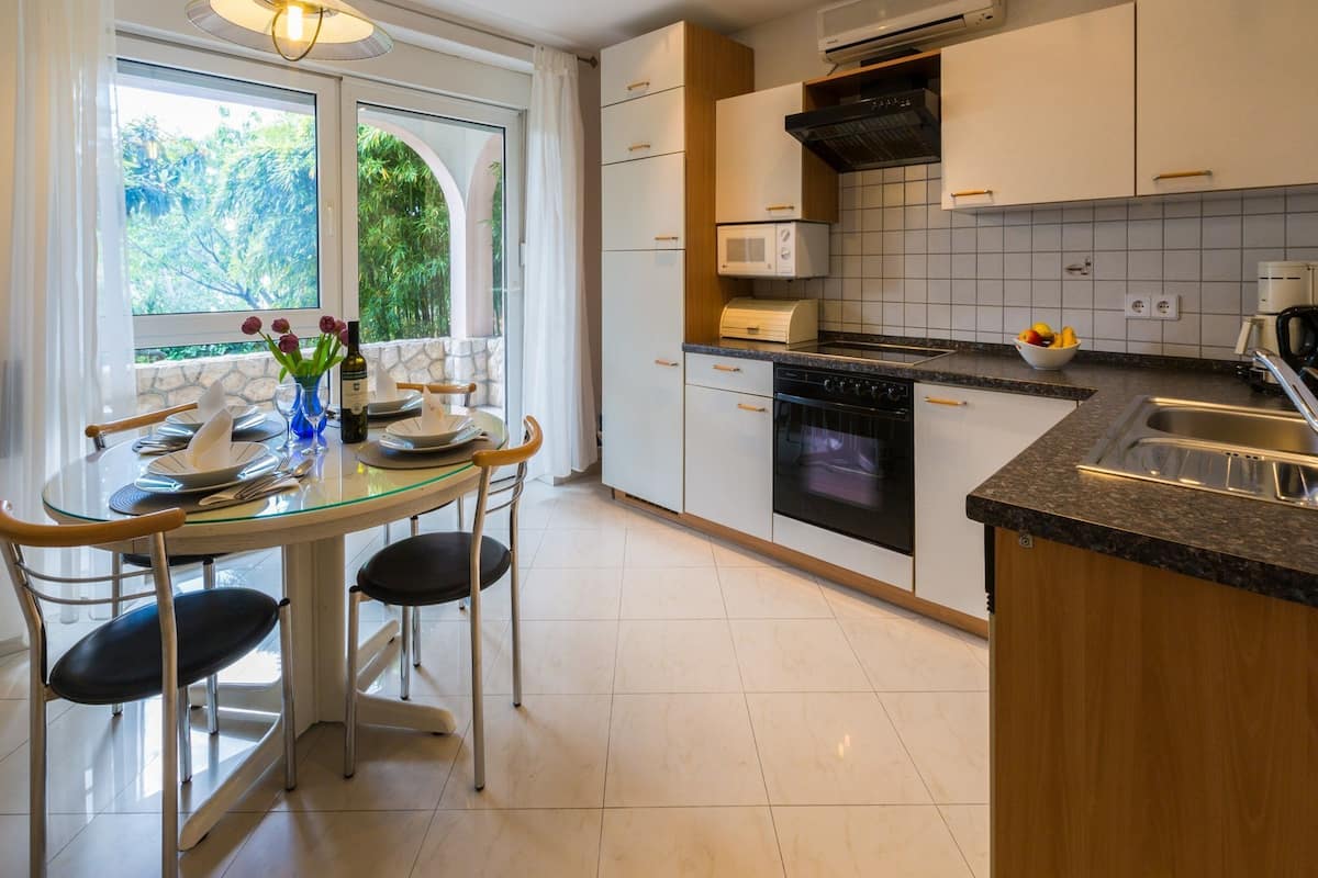 Een moderne keuken met een eethoek, met een glazen tafel, stoelen, een fornuis, magnetron en een spoelbak.
