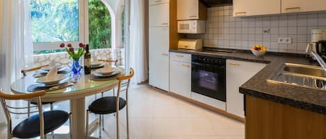 A modern kitchen with a dining area, featuring a glass table, chairs, a stove, microwave, and a sink.