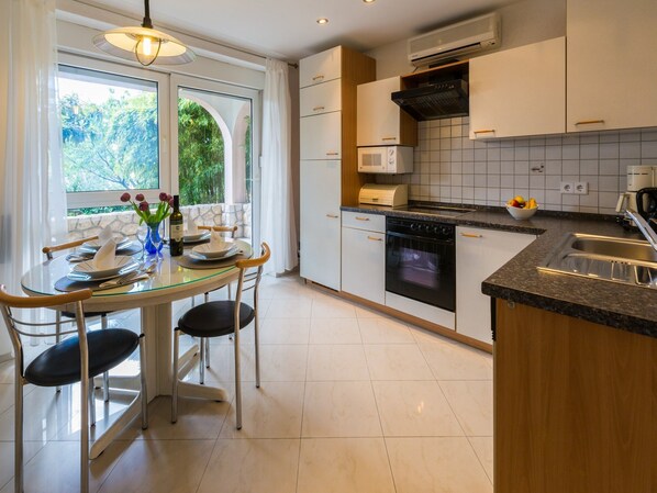 A modern kitchen with a dining area, featuring a glass table, chairs, a stove, microwave, and a sink. - Apartments Vanessa (Crikvenica)