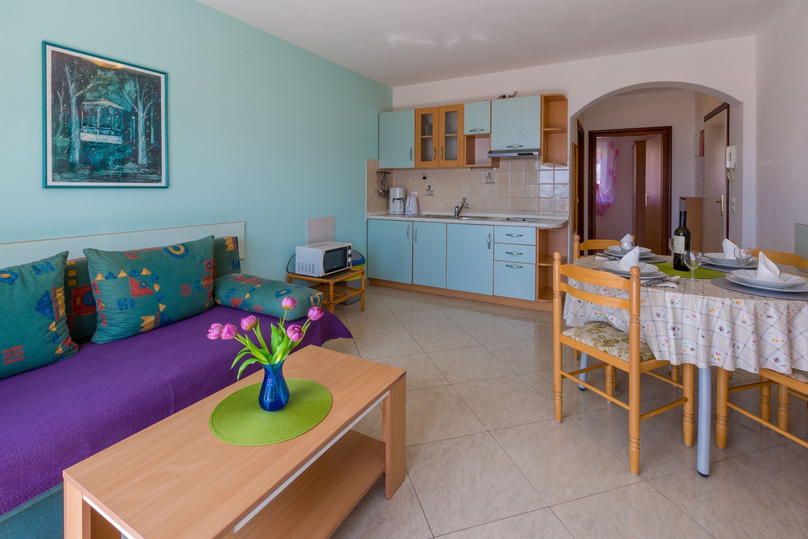 A compact living space with a kitchenette, a dining area, and a sofa with colorful cushions.