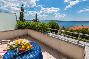 A balcony with a table set for breakfast, overlooking a scenic view of the sea and hills. - Apartments Vanessa (Crikvenica)