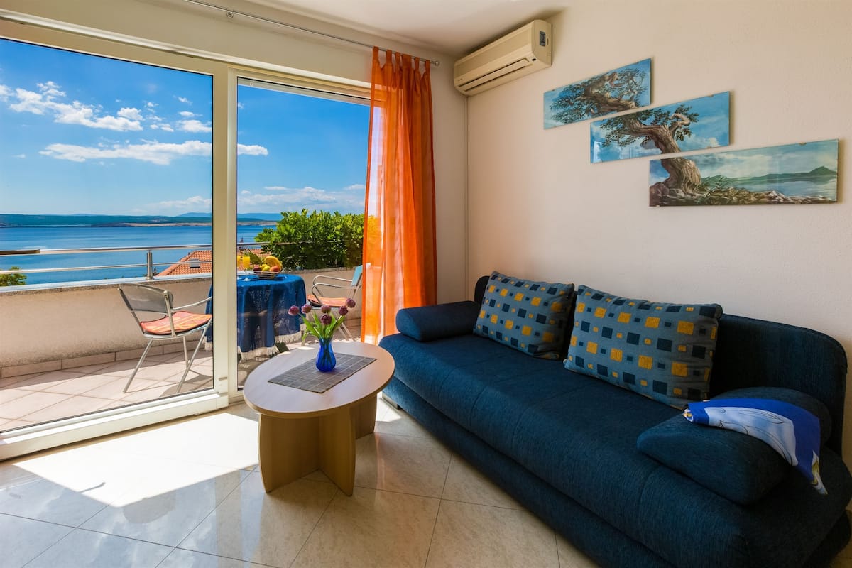 Een zithoek met een bank, een tafel met een vaas en uitzicht op zee vanaf een balkon.