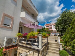 A building with a balcony, outdoor seating area with a purple umbrella, and a staircase leading to the entrance. - Apartments Vanessa (Crikvenica)