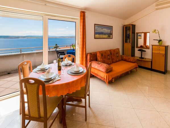 A dining area with a table set for two, a sofa, and a view of the sea. - Apartments Vanessa (Crikvenica)