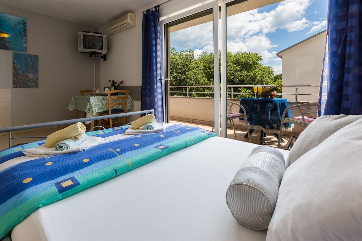 Een hotelkamer met een bed, een balkon met een tafel en stoelen, en een aan de muur bevestigde televisie.