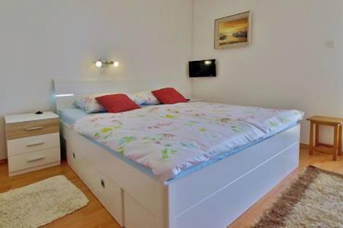 Ein Schlafzimmer mit einem Bett, einem Nachttisch, einem Teppich und einem Bild an der Wand.