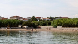 Blick auf einen Fluss mit Sandstrand, einigen Personen und Häusern im Hintergrund.