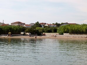 A riverside area with a sandy beach, a few people, and buildings in the background. - Apartments Anamari (Rab)