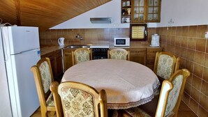 Eine Küche mit rundem Tisch, Holzsesseln, einem Kühlschrank, einer Mikrowelle und einem Schrank.