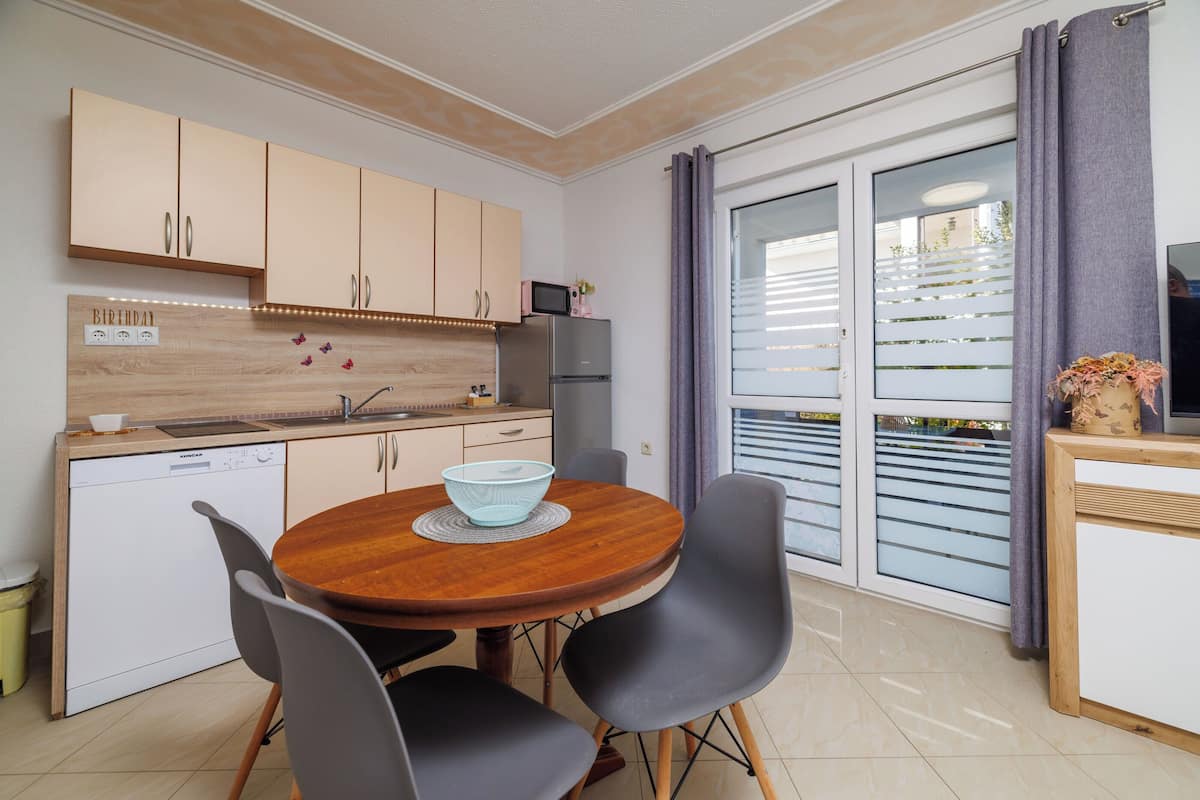 A compact kitchen with a wooden dining table, black chairs, and a built-in dishwasher.