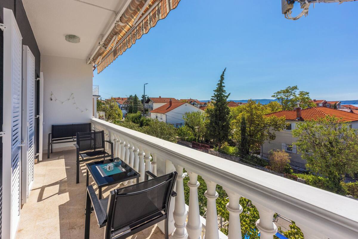 A balcony with a table and chairs, a view of houses and trees, and a clear blue sky.