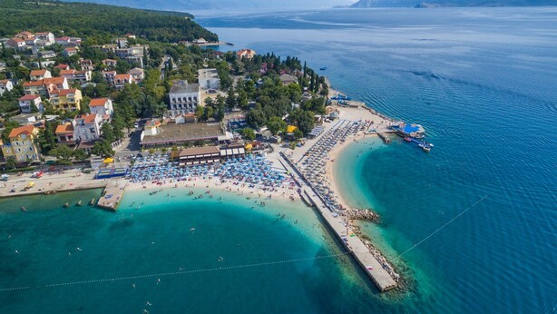 Una vista aerea di una località costiera con spiaggia, un molo e un hotel.