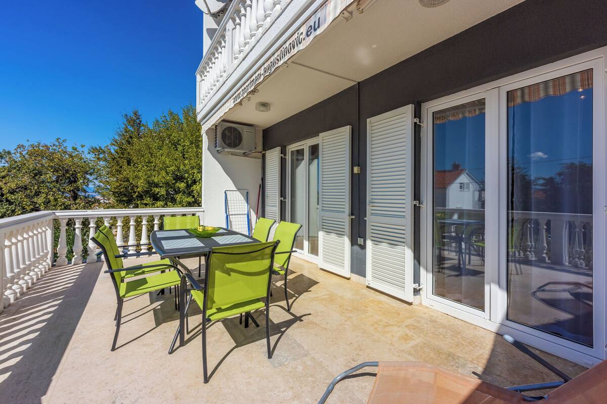 A balcony with a table and chairs, a white railing, and a view of the surrounding area.
