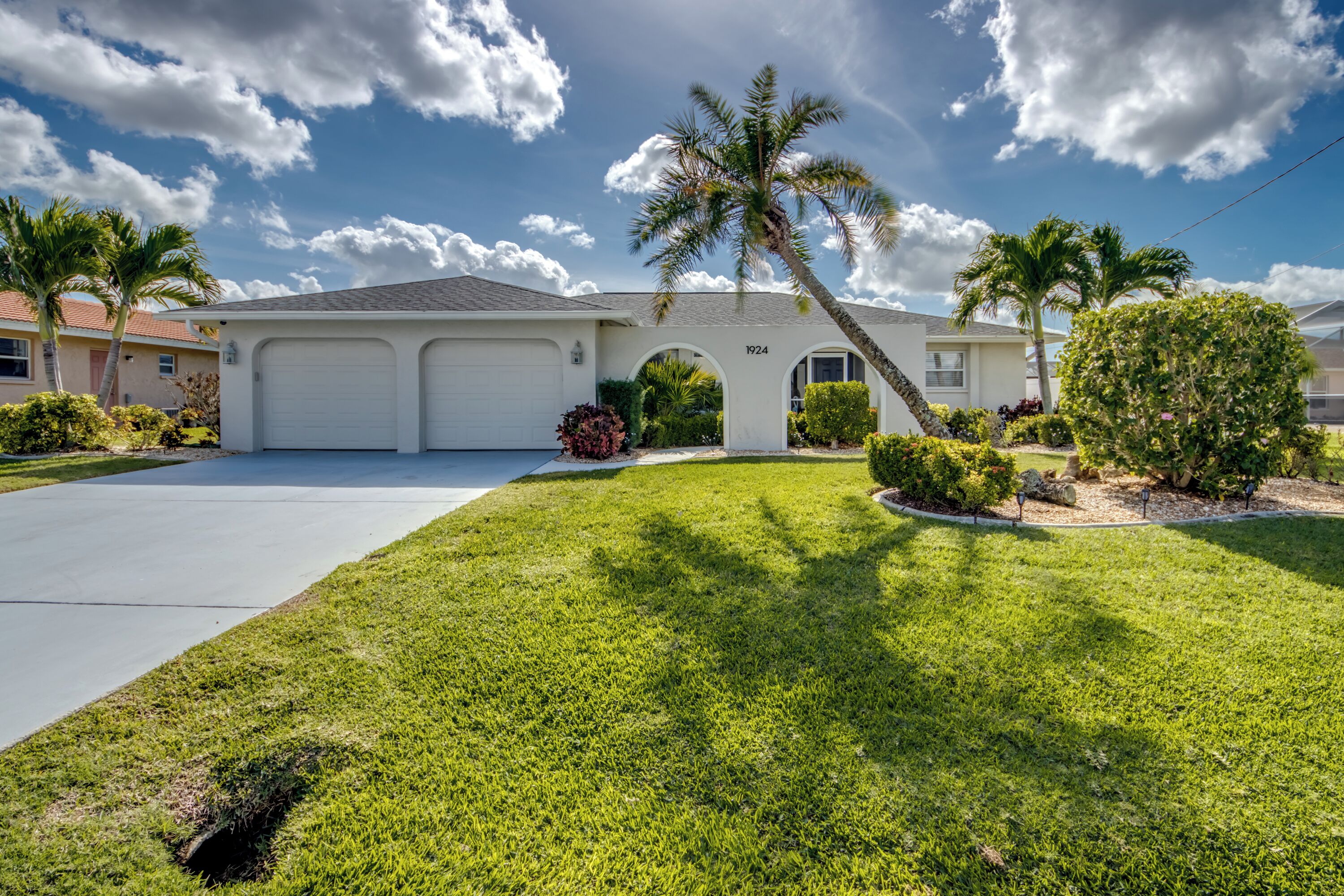 A single-story house with a garage, a well-maintained lawn, and palm trees.