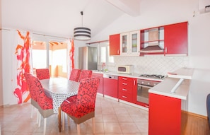 A modern kitchen with red cabinets, a dining table with patterned chairs, and a visible stove. - Apartments Mihaela (Pasman)