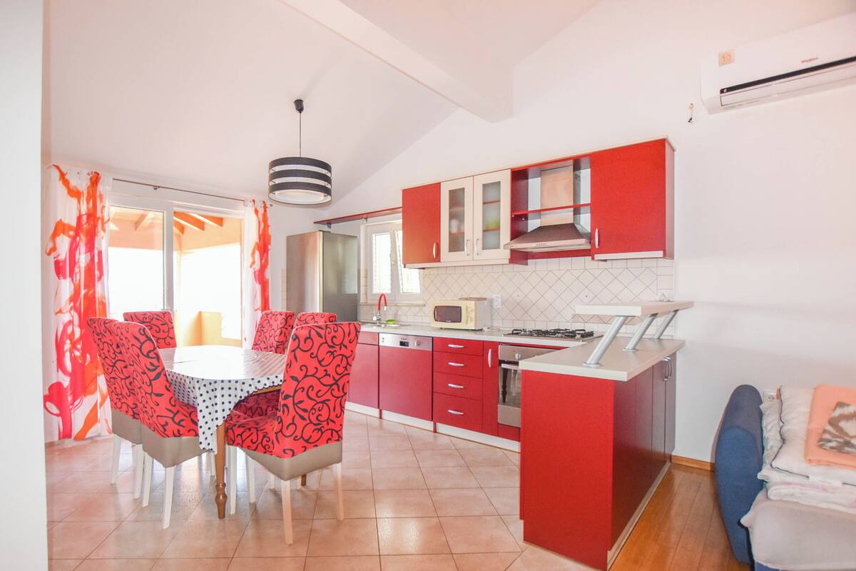 Une cuisine moderne avec des meubles rouges, un plan de travail blanc et un coin repas doté de chaises à motifs.