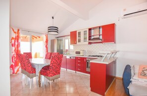 A modern kitchen with red cabinets, a white countertop, and a dining area with patterned chairs. - Apartments Mihaela (Pasman)