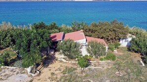 Une propriété située sur la côte, avec un bâtiment à toit rouge entouré d’une végétation luxuriante et offrant une vue dégagée sur la mer.