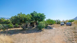 Une propriété rurale avec une maison en pierre, deux voitures garées et un ciel dégagé.