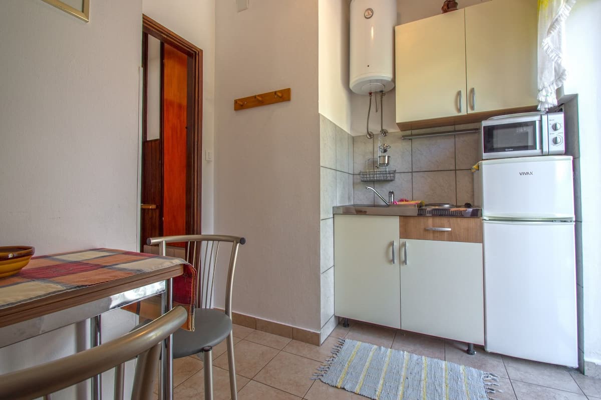 Una cucina compatta con microonde, frigorifero e scaldabagno. C'è un tavolo da pranzo con sedie e un tappeto sul pavimento.