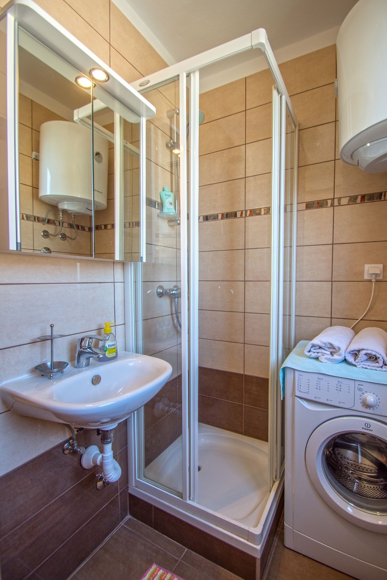 Un baño con ducha de vidrio, lavabo y lavadora.