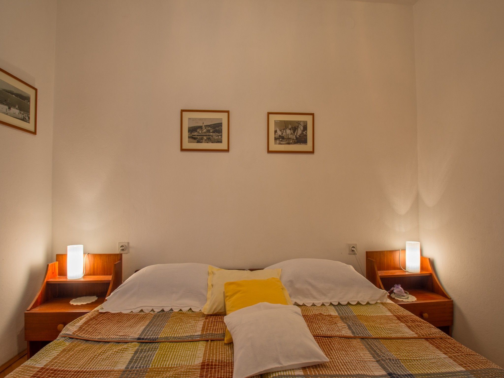 Une chambre à coucher comprenant un lit, deux tables de chevet, deux lampes fixées au mur et deux tableaux encadrés accrochés au mur.
