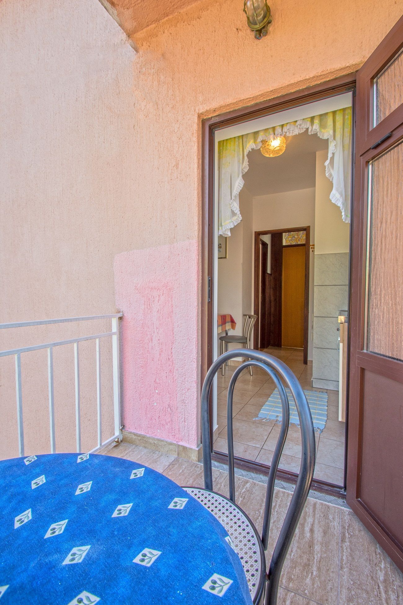 En lille balkon med et blåt bord og stole, gelænder og udsigt ind til bygningen.