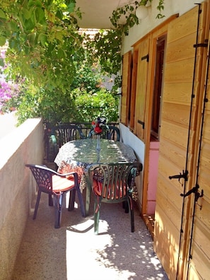 Un patio al aire libre con una mesa redonda y sillas, rodeado por una valla de madera y cubierto por una enredadera frondosa.