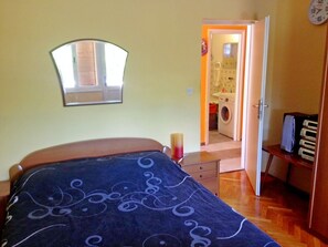 Un dormitorio con cama, un espejo, una puerta que da a un baño y una mesita con lámpara.
