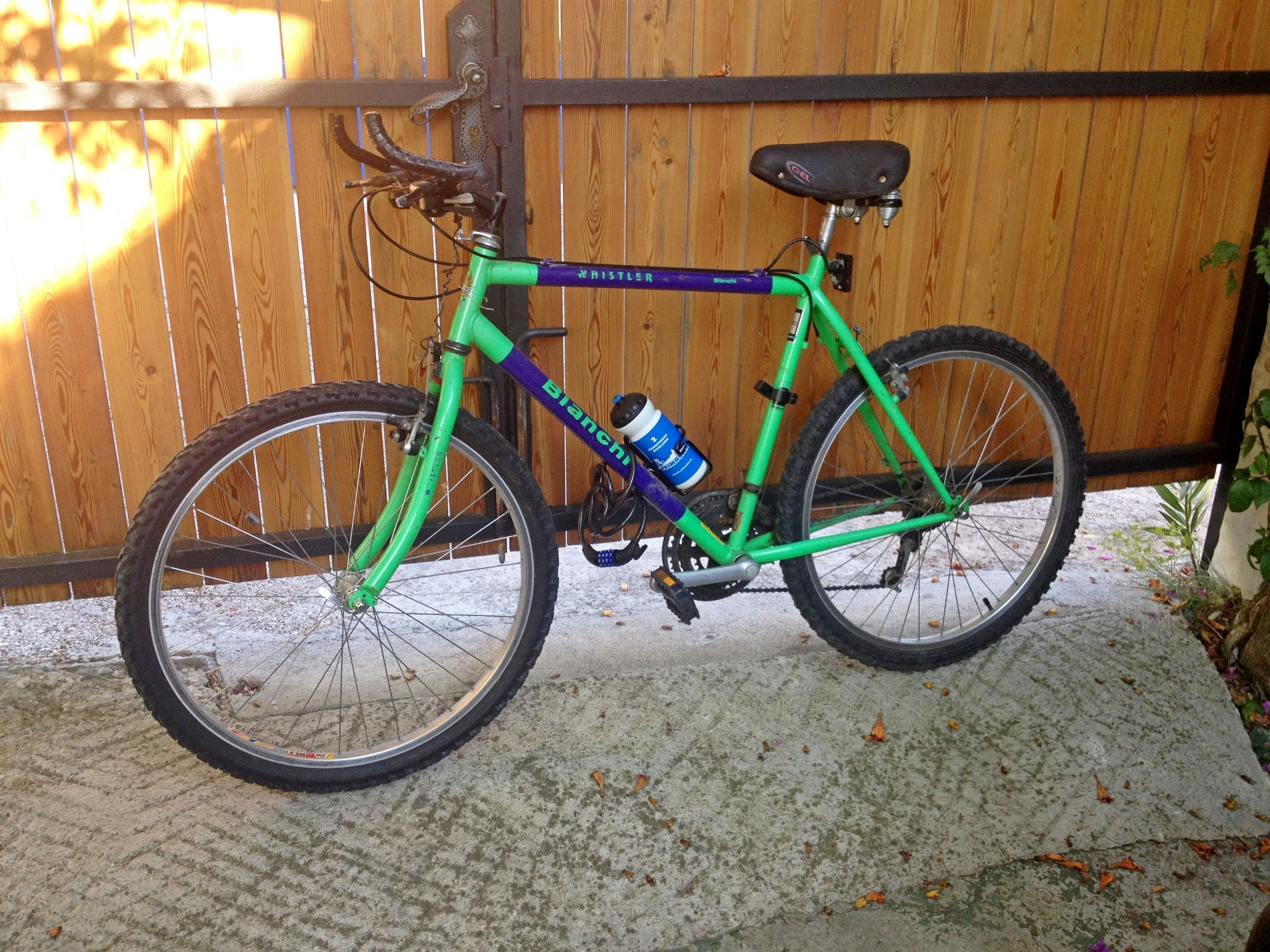 A green bicycle with a water bottle attached to the frame, parked against a wooden fence.