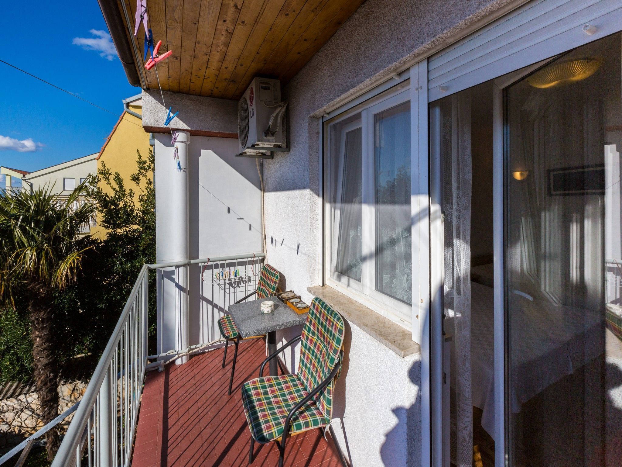 A balcony with a table and chairs, a hanging laundry rack, and a window with blinds.