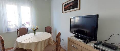 A dining area with a round table, chairs, a television, and a cabinet with drawers.
