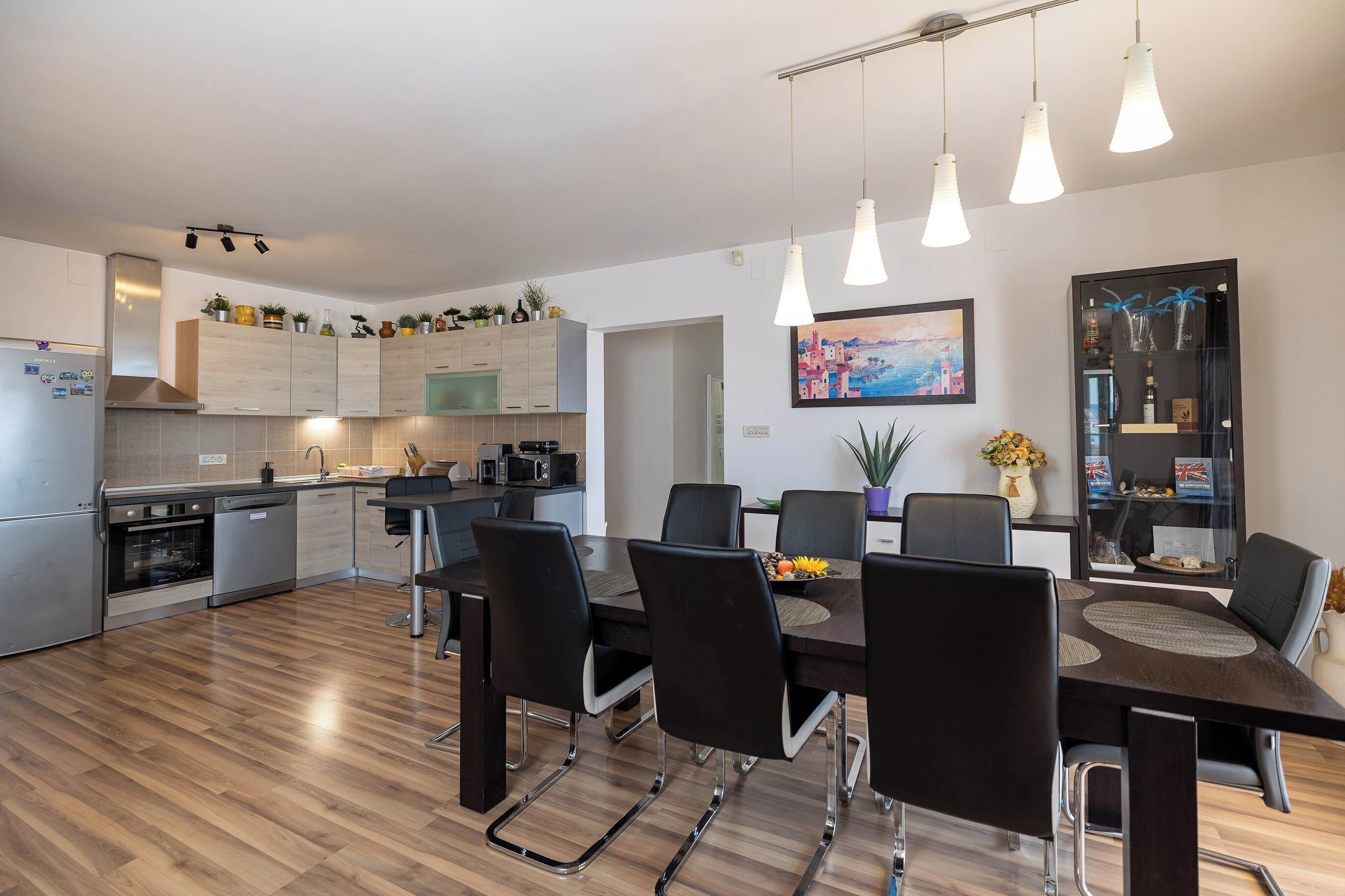 A modern kitchen with stainless steel appliances, a dining area with a dark wooden table and black chairs, and pendant lighting.