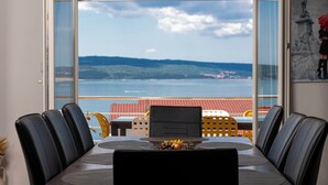 A dining area with a table set for six, overlooking a scenic view of the sea and hills. - Apartments Novoselic (Crikvenica)