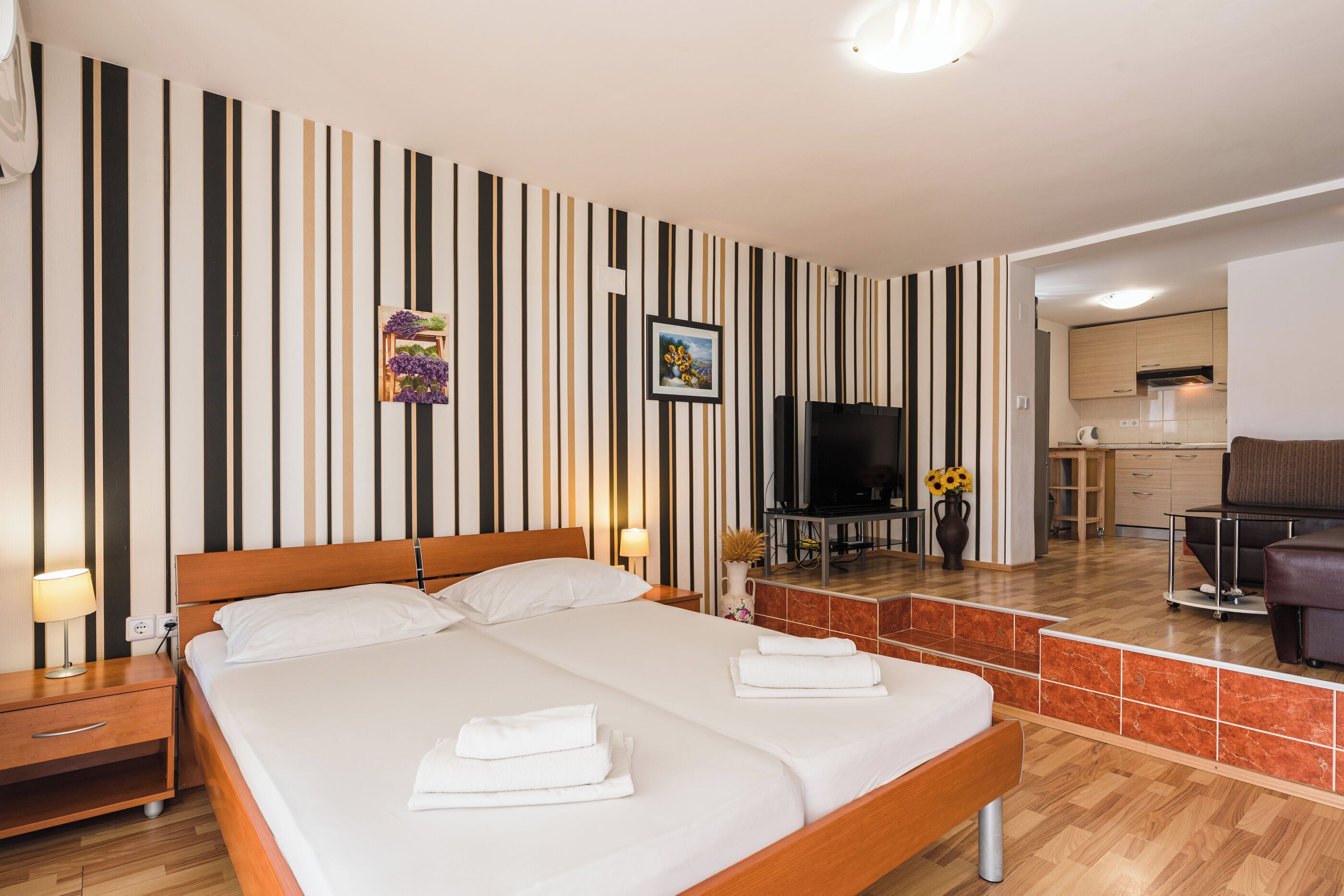 A hotel room with a large bed, a TV, a desk, and a kitchenette.