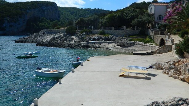 A coastal area with a concrete pier, boats, and a building with a stone wall. - Apartment Martina (Jelsa)