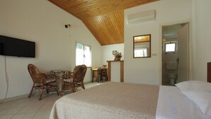A bedroom with a large bed, wooden ceiling, a flat-screen TV mounted on the wall, a small table with chairs, and a window. - Apartment Martina (Jelsa)
