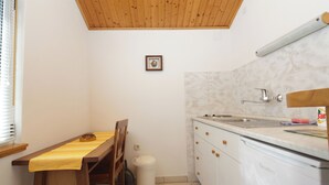 A small kitchen with a wooden table, chairs, a dishwasher, and a window with blinds. - Apartment Martina (Jelsa)