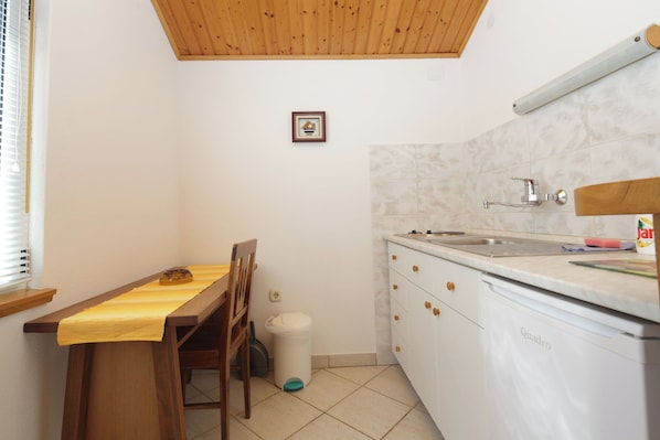 A small kitchen with a wooden table, chairs, a dishwasher, and a window with blinds. - Apartment Martina (Jelsa)