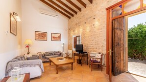 A cozy living room with a stone wall, a wooden door, a sofa, a coffee table, and a television. - Agrotourism "Es Rafalet - Casa Amitger" countryside views, pool, Wi-Fi, A/C, and garden (Manacor)