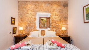 A double bed with a stone wall backdrop, two bedside tables with lamps, and a window with a view. - Agrotourism "Es Rafalet - Casa Amitger" countryside views, pool, Wi-Fi, A/C, and garden (Manacor)