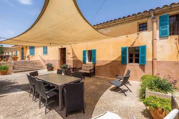An outdoor patio with a table and chairs, a covered seating area, and a building with blue shutters.