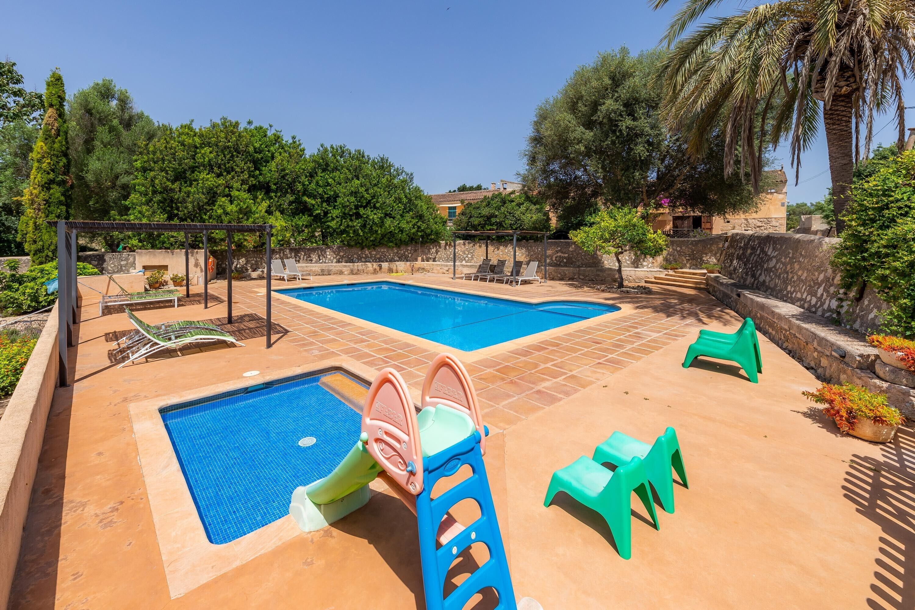 Una piscina con tobogán, sillas de descanso y una pérgola.
