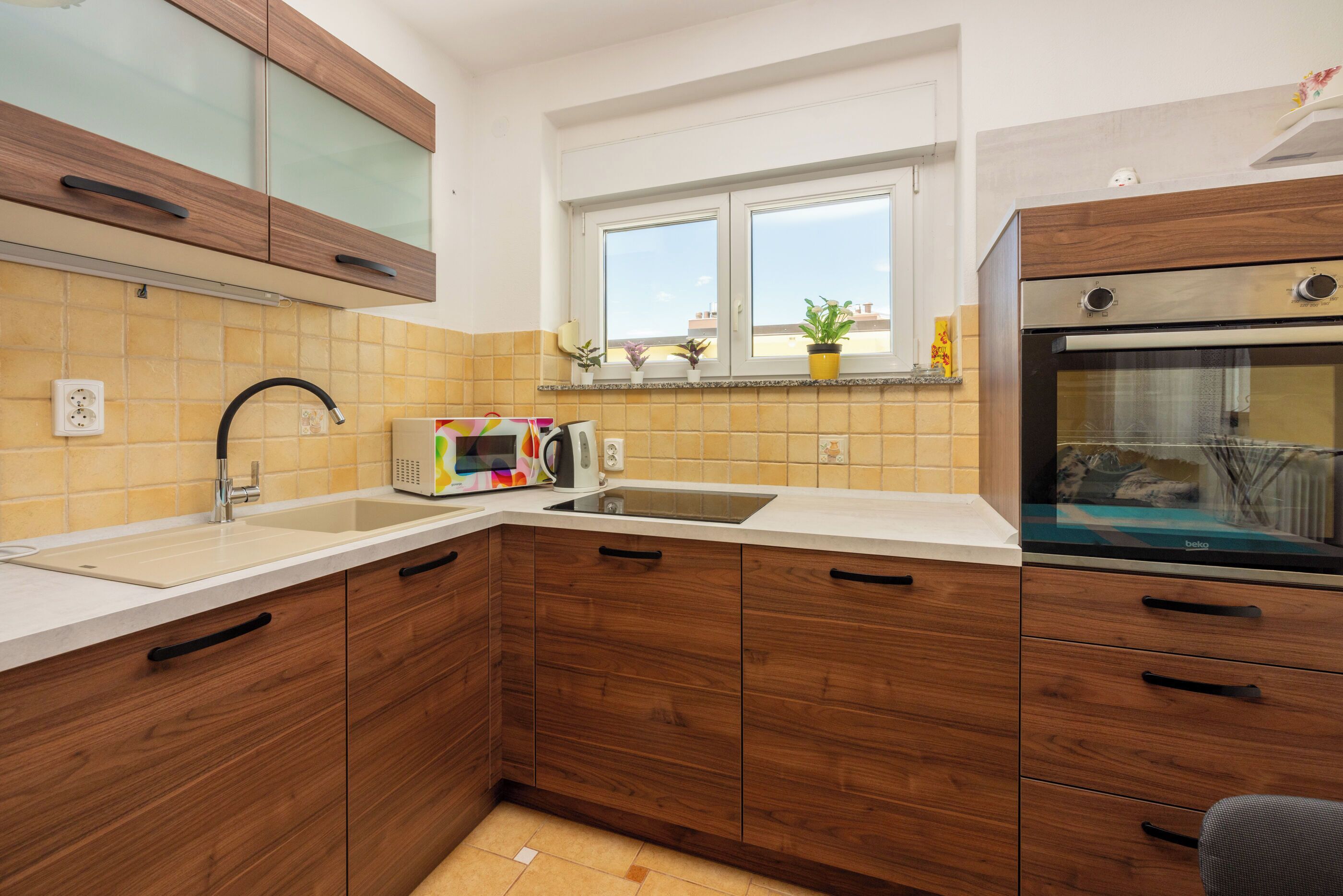 A modern kitchen with wooden cabinets, a built-in oven, and a window with potted plants.