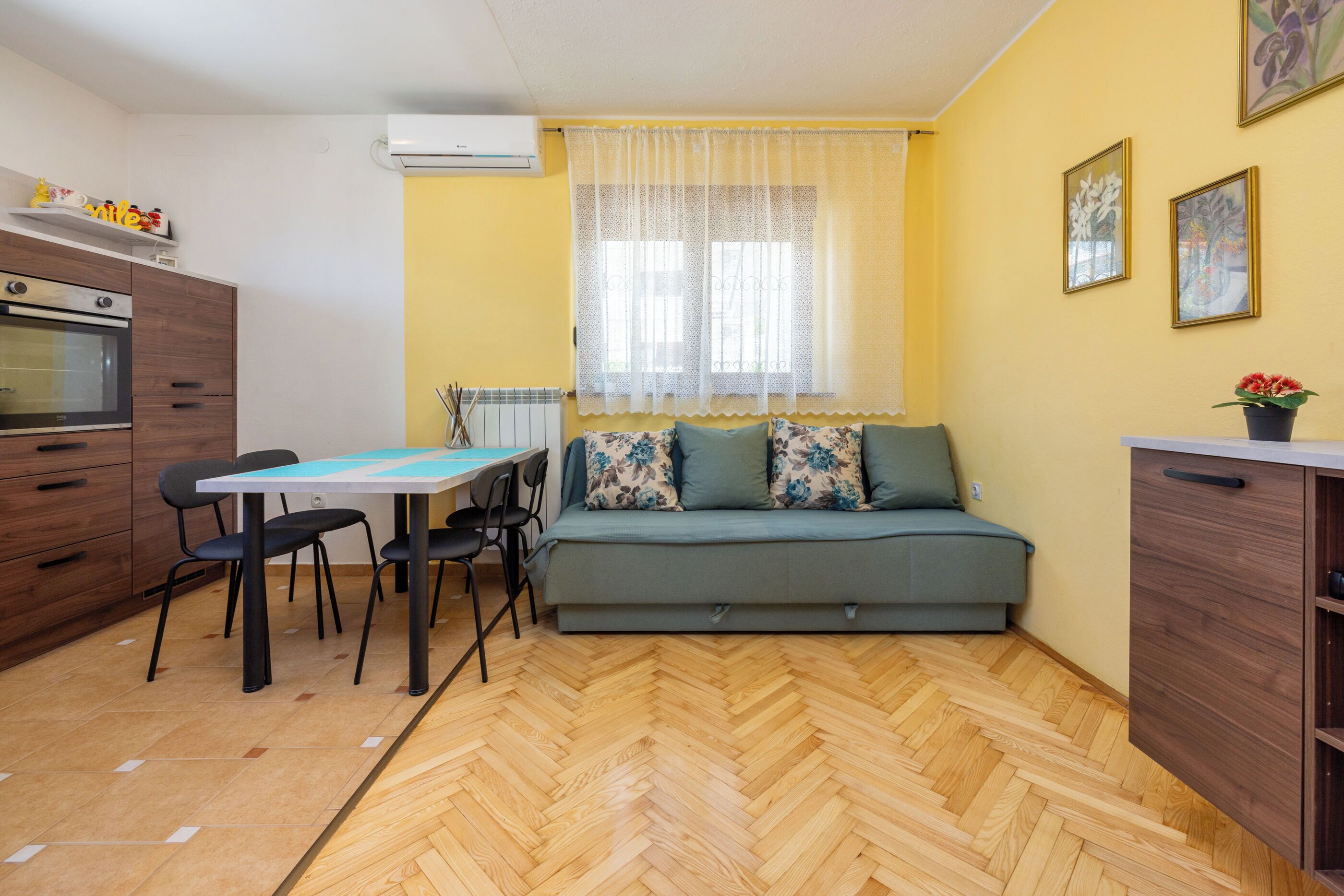 A compact living space with a kitchenette, a dining area, and a sofa with floral cushions.