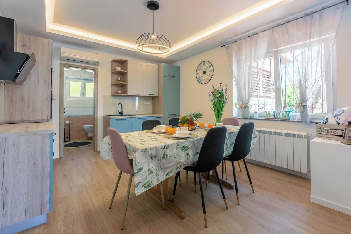 Una cucina moderna con zona pranzo, con orologio sulla parete, una finestra con tende e un tavolo apparecchiato per due.