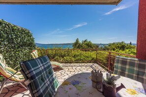 Un balcone con vista sul mare, un tavolo con tovaglia fiorata e due sedie con cuscini a quadri.