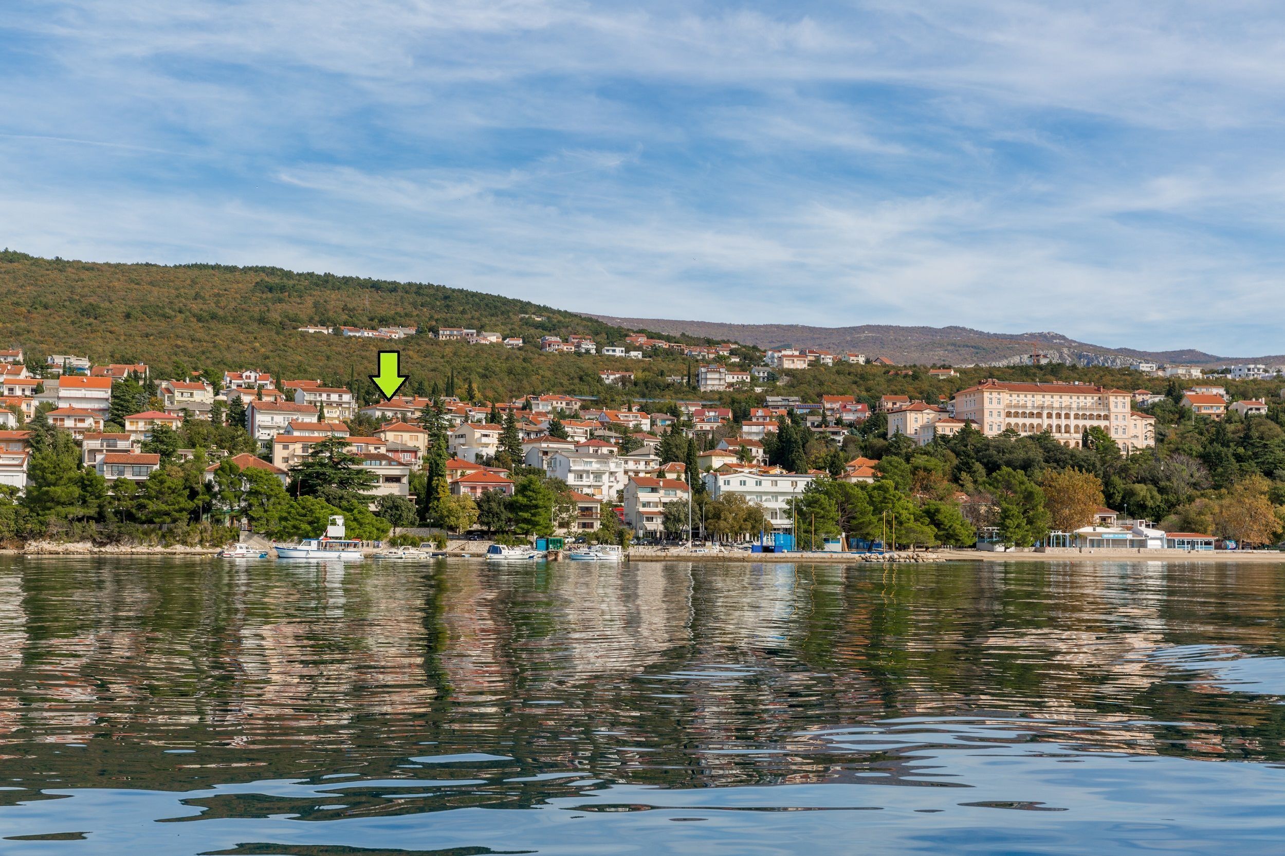 A coastal town with buildings along the waterfront, a body of water reflecting the structures, and a hill in the background.
