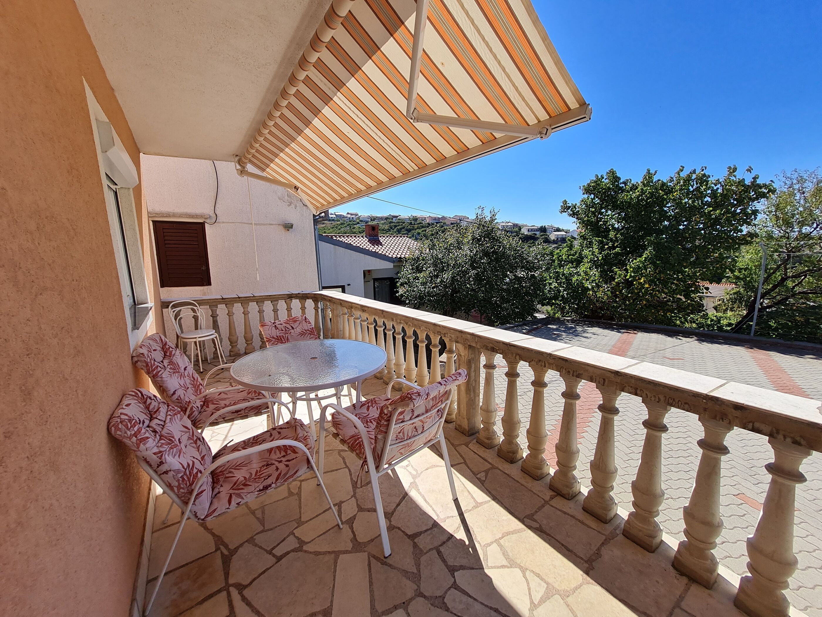 A balcony with a table and chairs, a striped awning, and a view of the surrounding area.